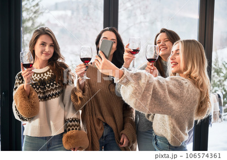 Young women enjoying winter weekends inside contemporary barn house. Four girls having fun, taking selfies on phone and drinking wine. Young women enjoying winter weekends inside contemporary barn house. Four girls having fun, taking selfies on phone and drinking wine. 106574361