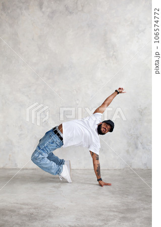 Man dancing break dance against background of gray wall in studio. Cool guy dancer, copy space Man dancing break dance against background of gray wall in studio. Cool guy dancer, copy space 106574772