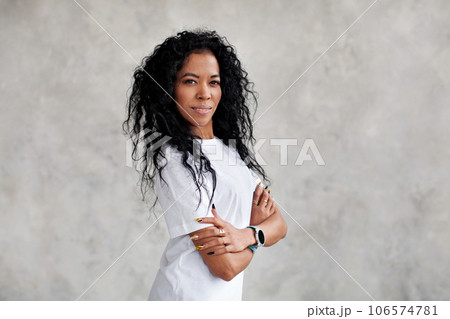 Portrait optimistic African American woman with long curly hair smiling, looking at camera, dressed in white T-shirt Portrait optimistic African American woman with long curly hair smiling, looking at camera, dressed in white T-shirt 106574781