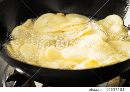 Potato slices being fried in a frying pan. 106575814