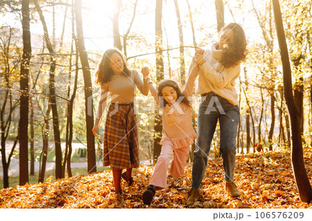 The homosexual family playing with her daughter in the autumn forest. The adventure is more fun. 106576209