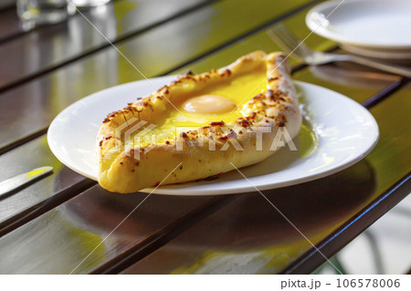 Adjara-style khachapuri, baked dough with egg, cheese and two pieces of butter on a white plate in a cafe. 106578006
