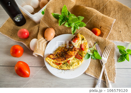 Stuffed omelette with tomatoes on a light wooden background. 106579120