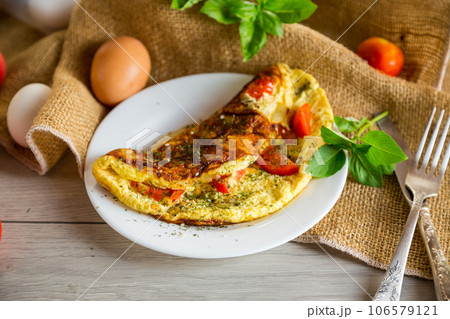 Stuffed omelette with tomatoes on a light wooden background. 106579121