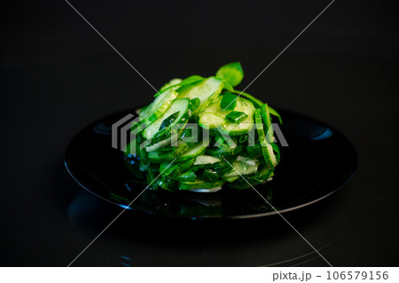 salad of fresh cucumbers with herbs and onions in a plate on a black background. 106579156