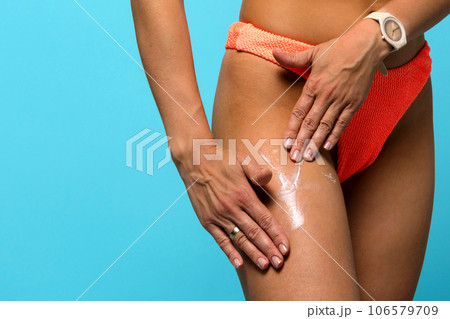 Woman in swimsuit applying moisturizing sunscreen cream to hip 106579709