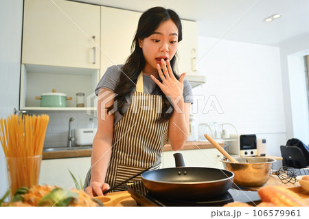 Cheerful asian housewife with spatula in hand, preparing breakfast in kitchen. People, food and domestic life concept 106579961