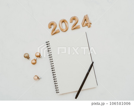 Flat lay of blank notebook sheet with copy space, numbers 2024, christmas decoration, christmas balls on white marble background Flat lay of blank notebook sheet with copy space, numbers 2024, christmas decoration, christmas balls on white marble background 106581006