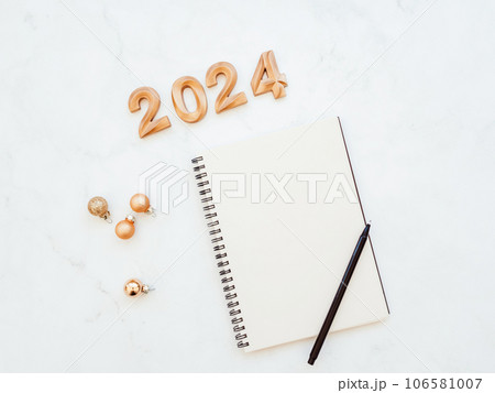 Flat lay of blank notebook sheet with copy space, numbers 2024, christmas decoration, christmas balls on white marble background 106581007