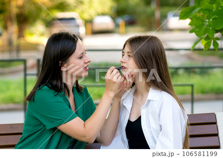 Mom applying lipstick to teenage daughter's lips Mom applying lipstick to teenage daughter's lips 106581199