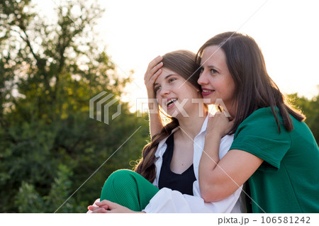Mom and teenage daughter hugging on walk in park Mom and teenage daughter hugging on walk in park 106581242