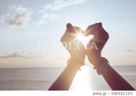 Woman holds hands up to sky in the shape of a heart 106582103