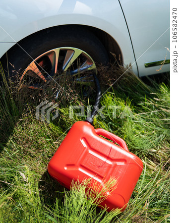 Red plastic canister among the green grass near the white car. Problems on the road with fuel for the car. 106582470