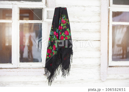 Russian national scarf hangs on the window of a wooden house.. Russian national scarf hangs on the window of a wooden house.. 106582651