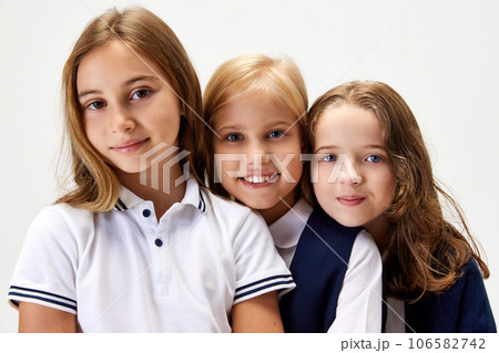 Three beautiful children, little girls, friends wearing school uniform, standing against white studio background Three beautiful children, little girls, friends wearing school uniform, standing against white studio background 106582742