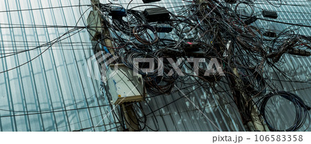 Tangled electrical wires and tangled communication lines on urban electric poles create a chaotic network. Disorganized and messy to organization management concept. Should take underground wire. 106583358