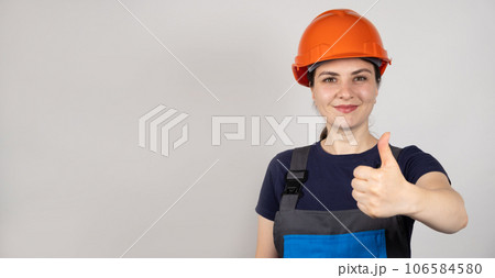 A woman in a protective helmet and overalls shows a thumbs up on a white banner background. 106584580