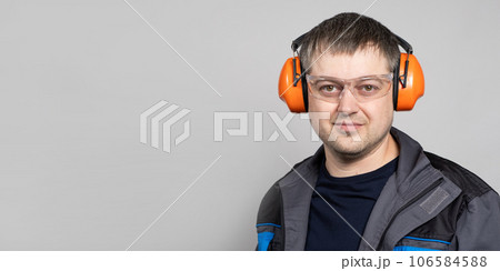 A man in earmuffs, glasses and overalls on a white background. 106584588