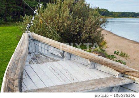 The nose of a wooden old boat painted with white paint on a green meadow on the lake The nose of a wooden old boat painted with white paint on a green meadow on the lake 106586256