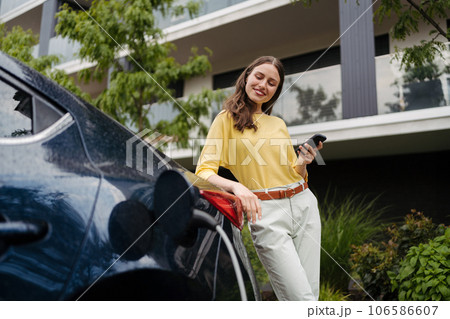 Smiling woman plugging charger in her electric car. 106586607