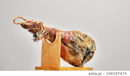 A front leg of Serrano ham mapped on a wooden stand on a white background. 106587474