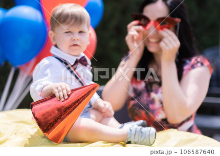 Stylish little boy gentleman celebrates first birthday in suspenders, joins his mother in celebrating his first year with a festive birthday party.balloons, party hats, and various other decorations. Stylish little boy gentleman celebrates first birthday in suspenders, joins his mother in celebrating his first year with a festive birthday party.balloons, party hats, and various other decorations. 106587640