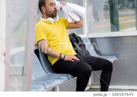 tired man portrait wiping sweat face with towel sitting in small arbor stadium after sport training athlete resting after hard workout on outdoor athletic arena 106587645