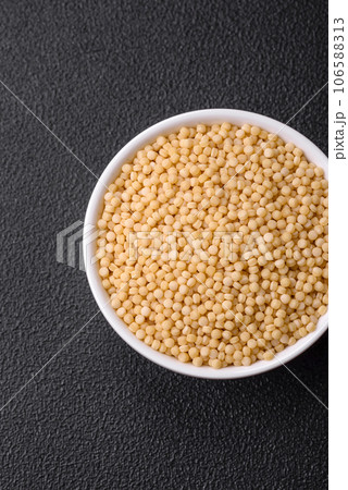 Raw ptitim pasta in a ceramic bowl on a dark concrete background 106588313