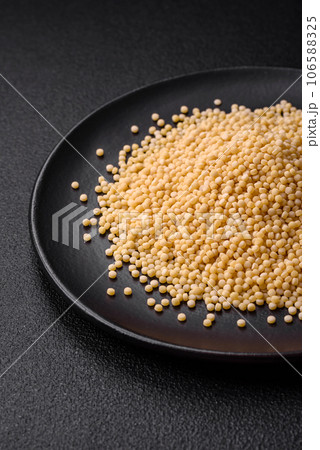 Raw ptitim pasta in a ceramic bowl on a dark concrete background 106588325