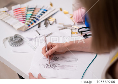 Designer draws future women dress sketch with pencil on paper working in fashion atelier skilled dressmaker creates new garment models at workplace in shop closeup Designer draws future women dress sketch with pencil on paper working in fashion atelier skilled dressmaker creates new garment models at workplace in shop closeup 106589266