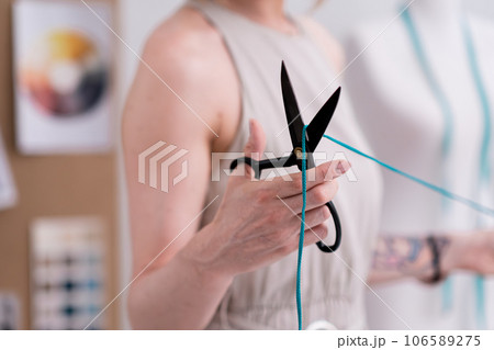 Woman tailor cuts green thread with sharp scissors in fashion atelier clothing designer works with sewing material for macrame craft in modern workshop closeup Woman tailor cuts green thread with sharp scissors in fashion atelier clothing designer works with sewing material for macrame craft in modern workshop closeup 106589275