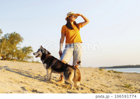 Woman in hat and sunglasses with her dog enjoying sunset on the beach Woman in hat and sunglasses with her dog enjoying sunset on the beach 106591774