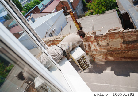 without a face. A man installs an external air conditioner. dangerous work. without a face. A man installs an external air conditioner. dangerous work. 106591892
