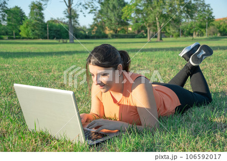 Caucasian Woman lying on park wearing light fitness clothing using laptop happy Caucasian Woman lying on park wearing light fitness clothing using laptop happy 106592017
