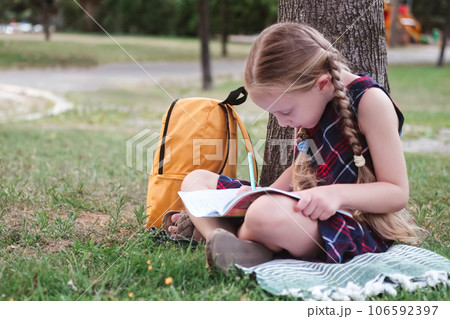 Nature's classroom: a happy schoolgirl studies beneath a tree in a green city park during a warm autumn day. Nature's classroom: a happy schoolgirl studies beneath a tree in a green city park during a warm autumn day. 106592397