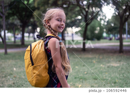 A schoolgirl in her dress and yellow backpack wears a joyful smile as she sets off for school, exuding happiness in her portrait.  106592446