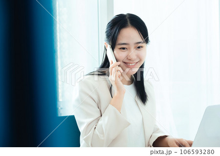パソコンの前でスマホで通話する若い女性 106593280