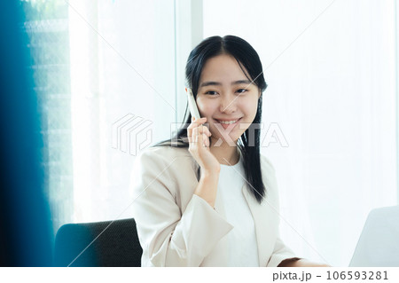 パソコンの前でスマホで通話する若い女性 パソコンの前でスマホで通話する若い女性 106593281