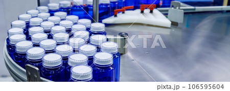 blue plastic bottle on production line of conveyor belt at filling machine in medical factory. pharmaceutical manufacturing. blue plastic bottle on production line of conveyor belt at filling machine in medical factory. pharmaceutical manufacturing. 106595604