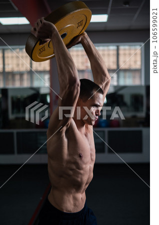 Muscular shirtless man doing exercise with weight plate in gym. Muscular shirtless man doing exercise with weight plate in gym. 106599021