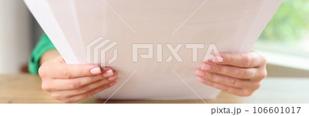 Woman sitting at table and holding sheets of paper Woman sitting at table and holding sheets of paper 106601017