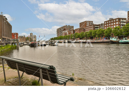 a bench on the side of a body of water with buildings in the background and boats parked along the shore a bench on the side of a body of water with buildings in the background and boats parked along the shore 106602612