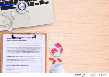 Laptop computer and pill with blue stethoscope on wooden desk. 106604133