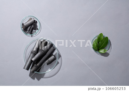 Activated charcoal sticks are contained inside petri dishes. Few green tea leaves featured. Vacant space to display product extracted from activated bamboo charcoal 106605253