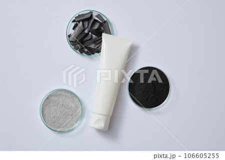Clay mask powder, black powder and activated bamboo charcoal are displayed inside petri dishes. Blank label tube for branding mockup design of activated bamboo charcoal extract 106605255