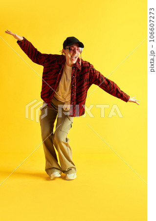 Full-length image of young woman in stylish sportive clothes dancing, having fun against yellow studio background. Style 106607273