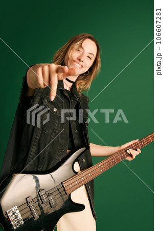 Portrait of young girl, musician in stylish clothes, making performance, playing electric guitar against green studio background Portrait of young girl, musician in stylish clothes, making performance, playing electric guitar against green studio background 106607281