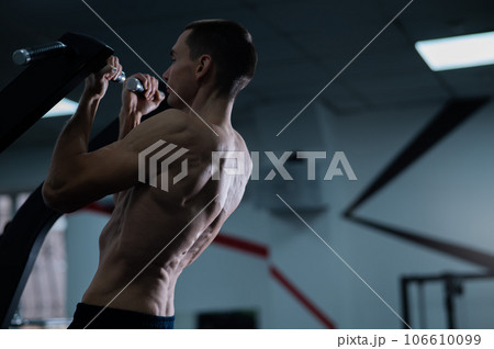 Back view of shirtless man with pull-ups in gym. Narrow grip. 106610099