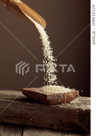Grains of white sesame are poured with a wooden spoon in the wooden dish. 106610126
