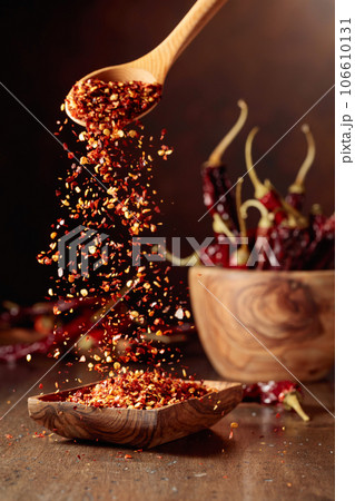 Chilli flakes are poured into a wooden dish. 106610131